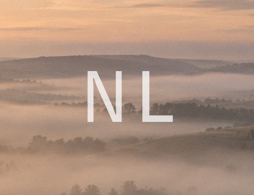 Nebelige Berglandschaft im warmen Morgenlicht mit weißem Schriftzug NL – DESOTO Retoureninformationen für die Niederlande.